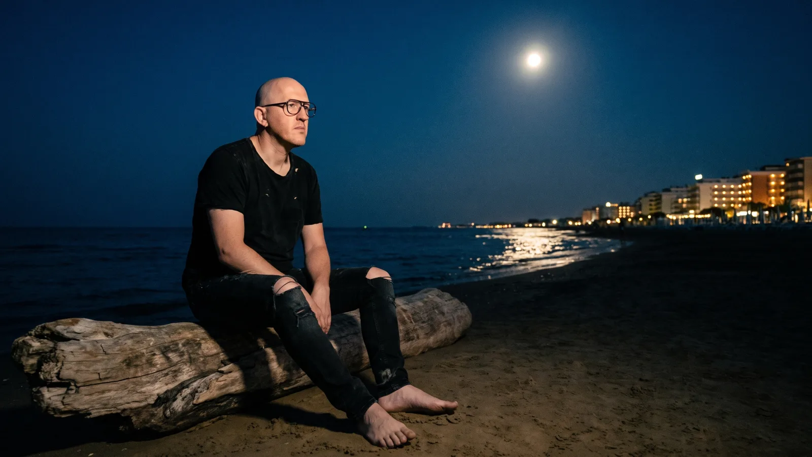 Marco Maso seduto in riva al mare di notte sotto la luna piena