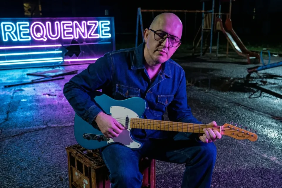 Marco Maso suona la Telecaster davanti all'insegna al neon di Frequenze